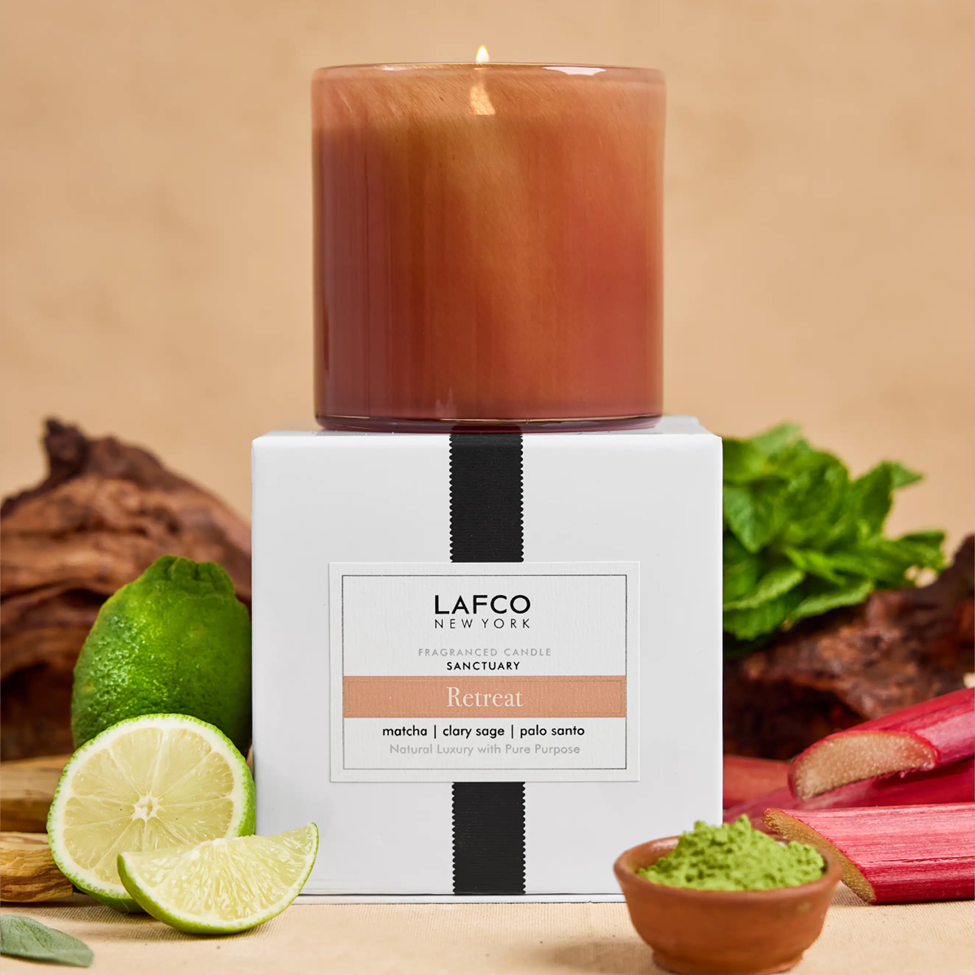 Lafco candle with packaging on a wooden surface with limes and rhubarb