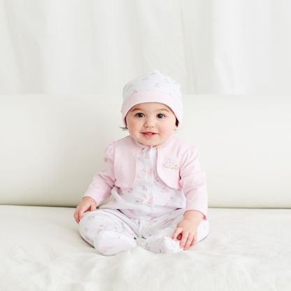 Baby in pink outfit and white hat sitting on a white surface