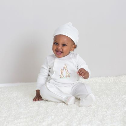 Baby in a white outfit with a letter 'A' design, sitting on a white surface.