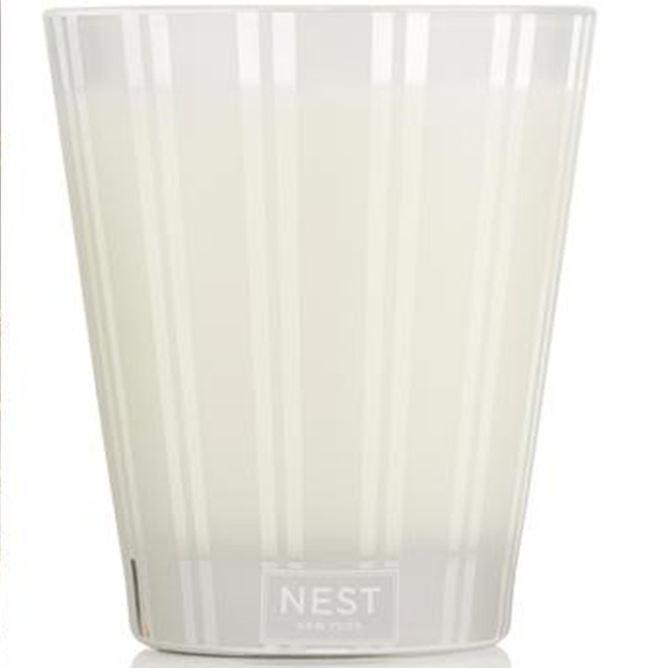 White candle in a glass container with 'NEST' branding on a white background