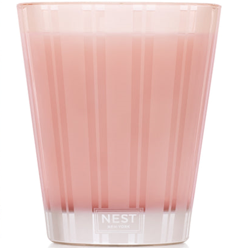 Pink candle in a glass container with 'NEST' branding on a white background