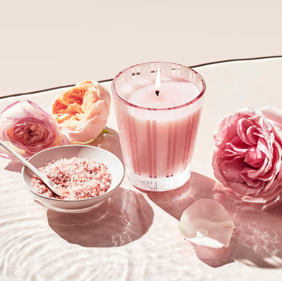 Pink candle with a bowl of pink salt and flowers on a white surface