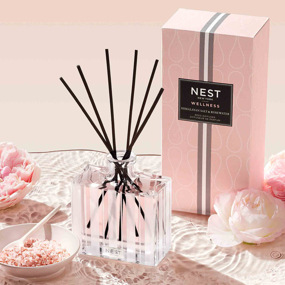 NEST wellness diffuser with packaging and flowers on a pink background