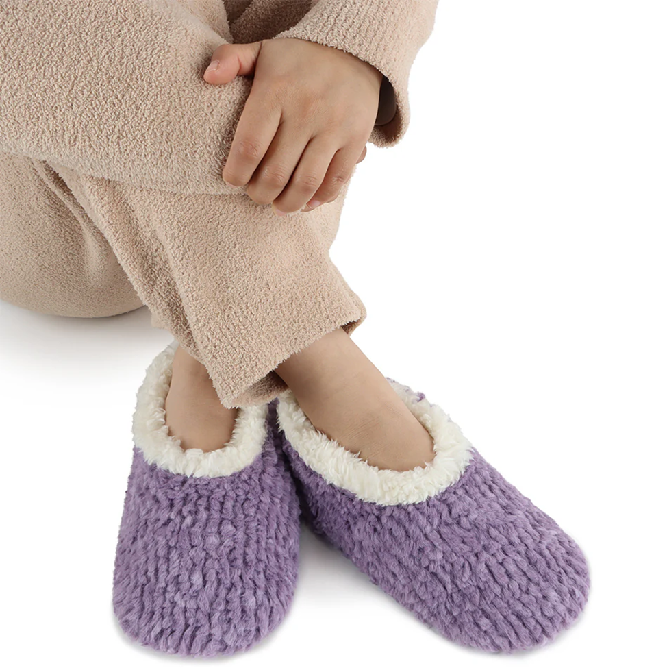 Purple fuzzy slippers worn with a beige robe on a white background