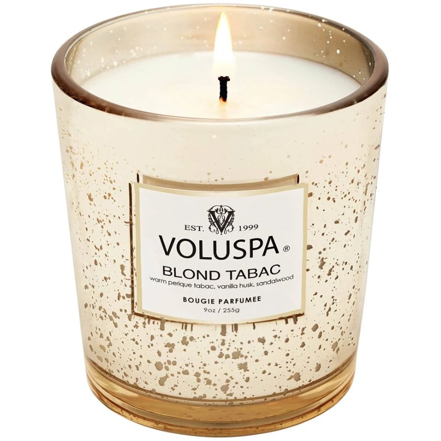 Lit Voluspa Blond Tabac candle in a decorative glass container on a white background