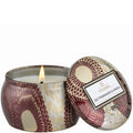 Decorative candle in a patterned tin with a lit flame on a white background