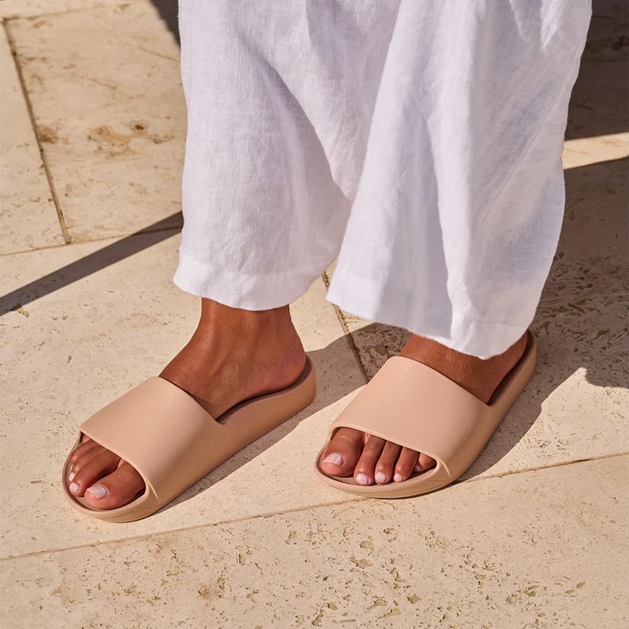 Beige sandals worn with white pants on a stone pavement