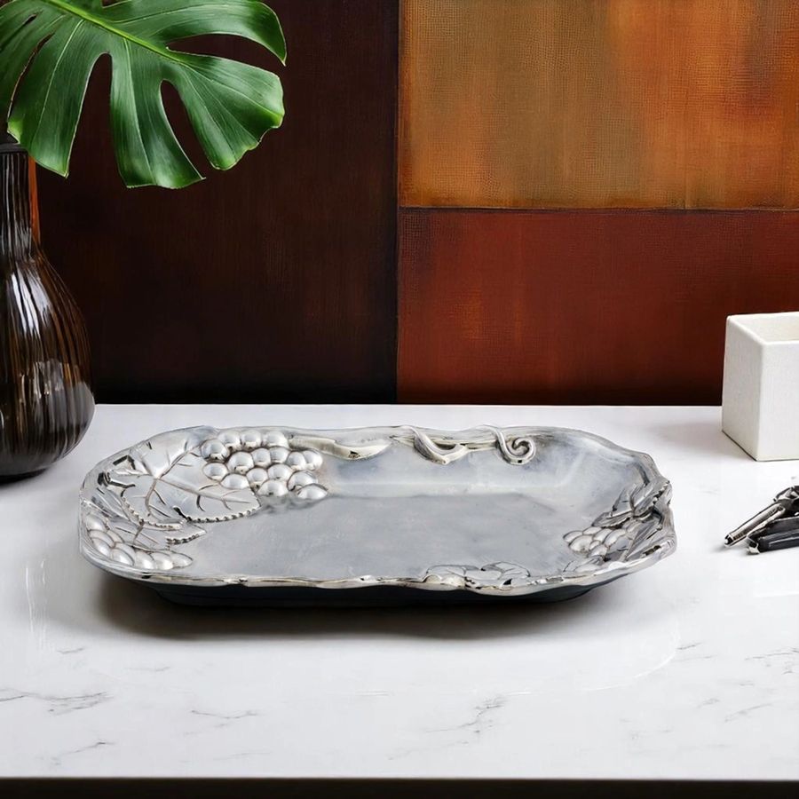 Decorative silver tray on a marble surface with a plant and vase in the background