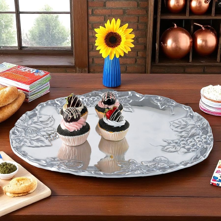 Decorative silver platter with cupcakes on a wooden table, sunflower in a blue vase.