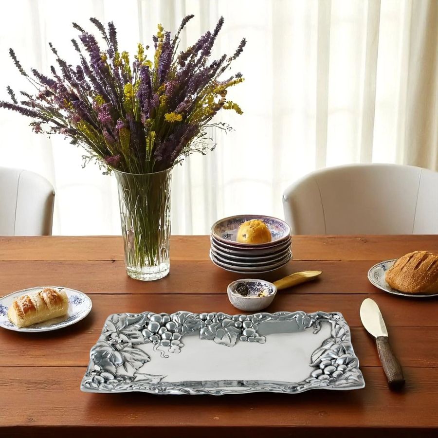 Decorative silver tray on a wooden table with a vase of flowers and plates of bread.