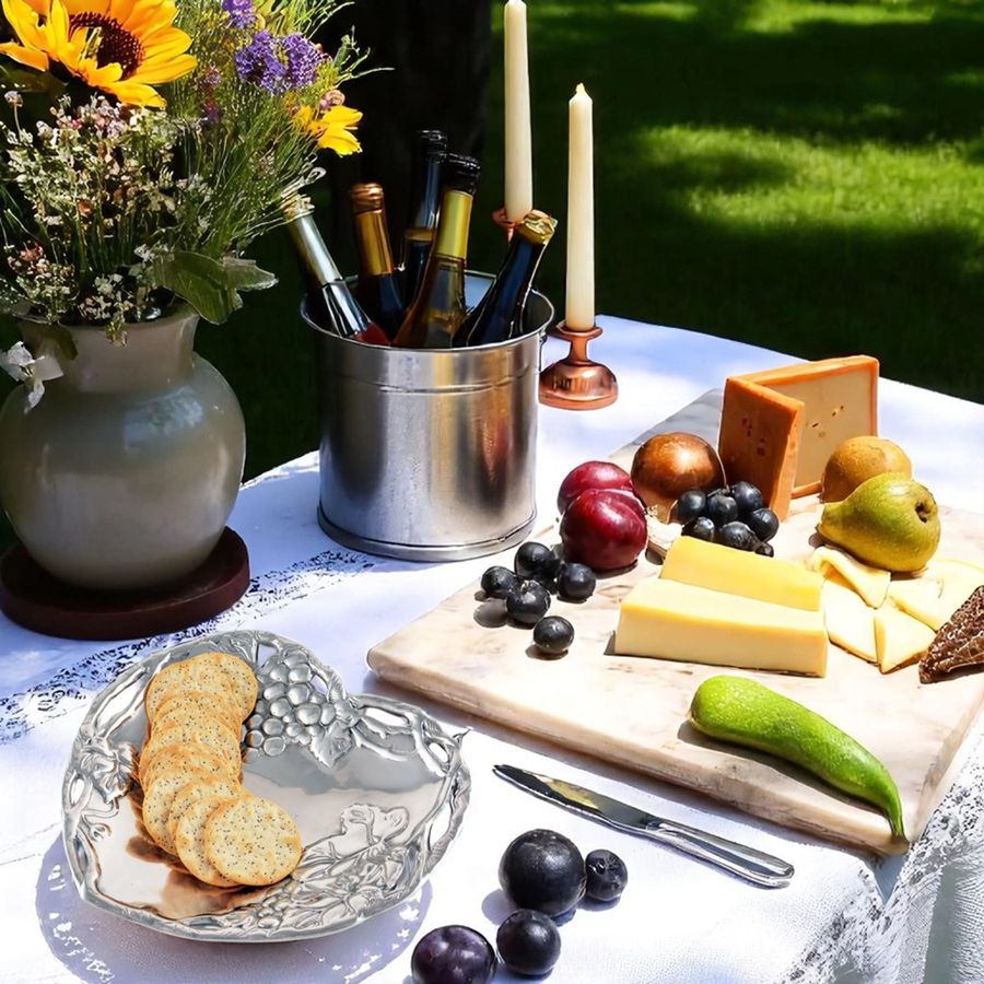 Outdoor setting with a cheeseboard, crackers, fruits, and candles on a tablecloth.