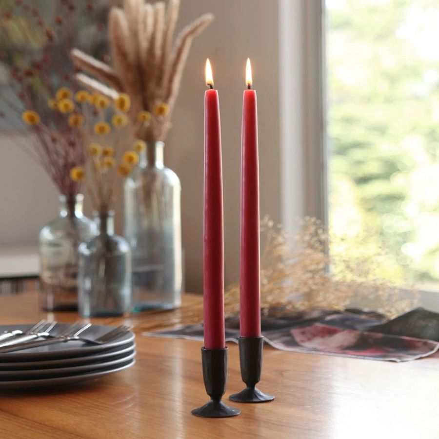 Two red candles in black holders on a wooden table with decorative elements.