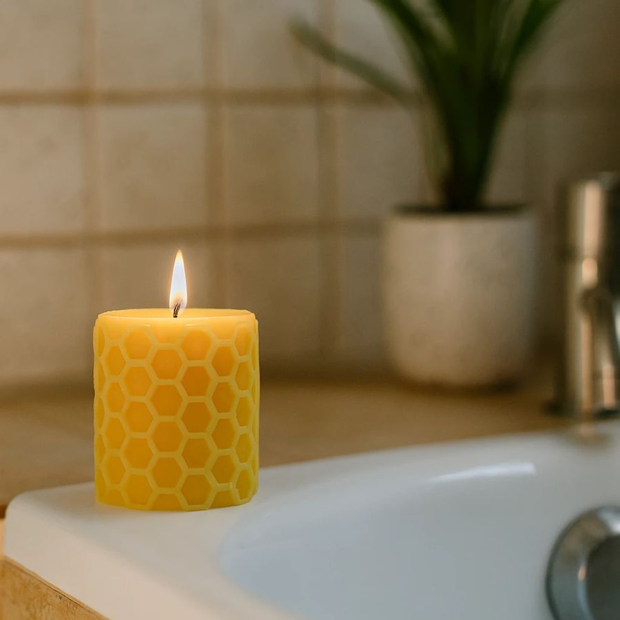 Yellow candle with honeycomb pattern on a bathroom counter, with a plant in the background.