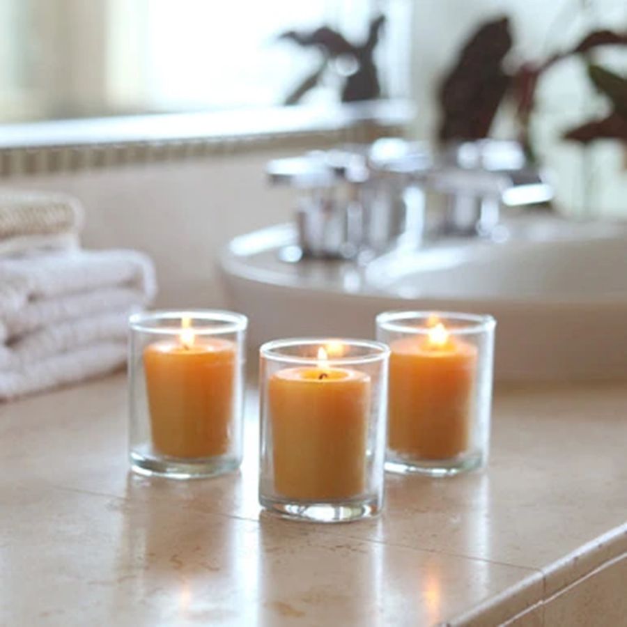 Three lit candles in glass holders on a bathroom counter with blurred background