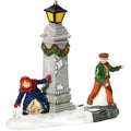 Decorative figurine of two people by a lamp post with snow and wreath decorations on a white background