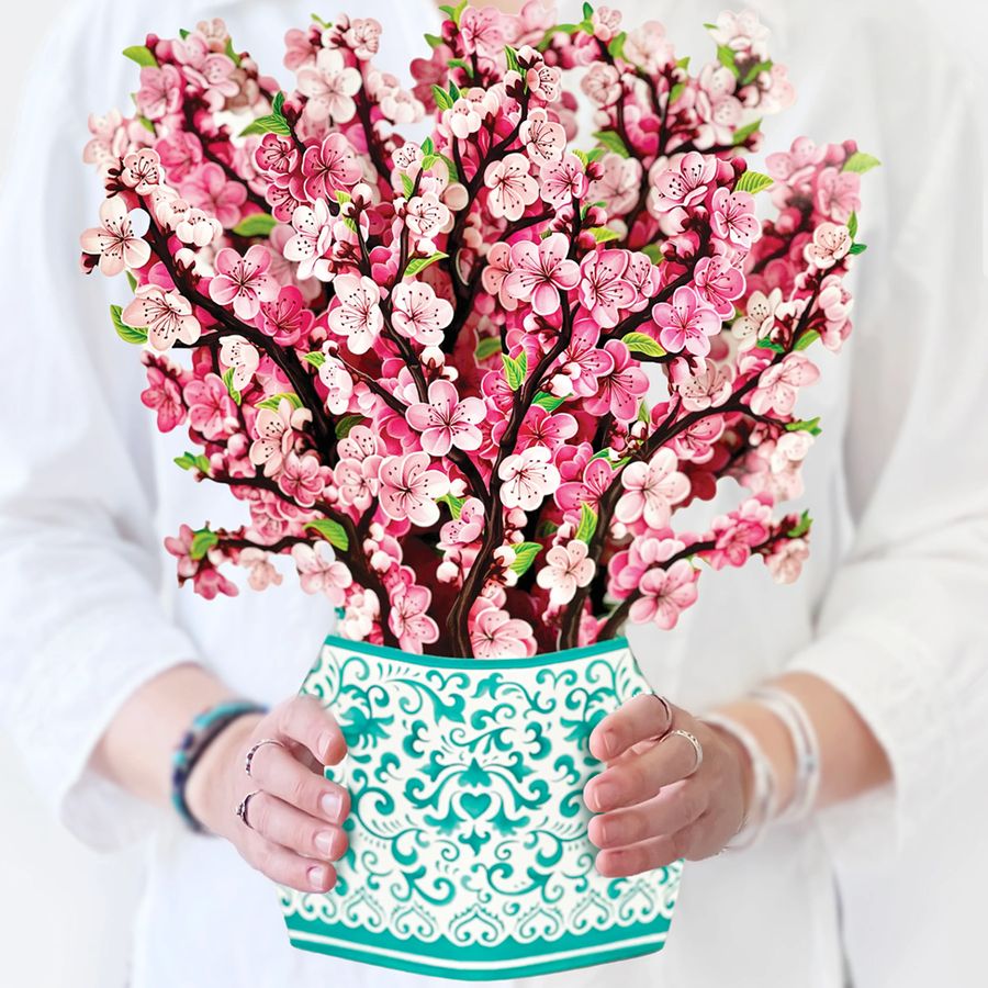 Bouquet of pink flowers in a decorative green and white container held by a person.