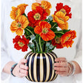 Bouquet of orange and red flowers in a striped vase held by a person.