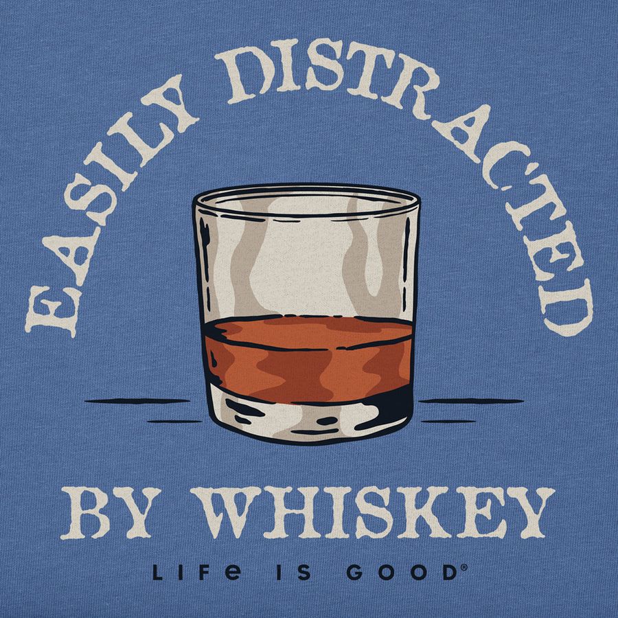 A graphic print on a heathered blue t-shirt featuring an illustration of a whiskey glass with amber liquid, surrounded by the text 'EASILY DISTRACED BY WHISKEY' and 'LIFE IS GOOD' in cream-colored lettering.