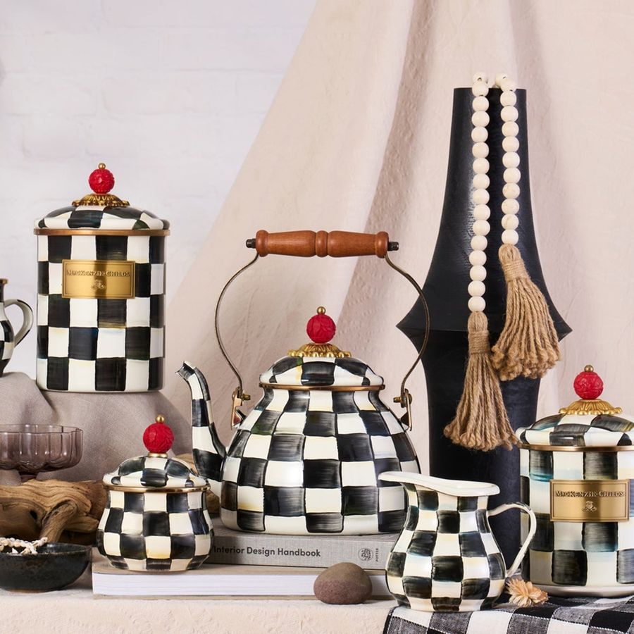 Black and white checkered teapot with wooden handle and red knobs, surrounded by decorative items.