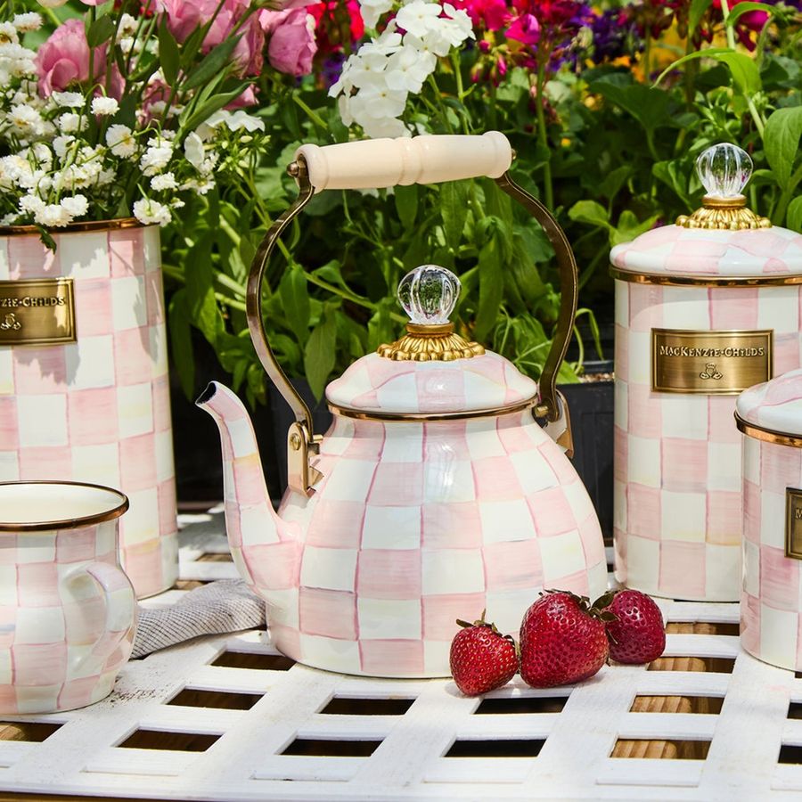Pink checkered teapot with matching mugs on a table with strawberries and flowers in the background