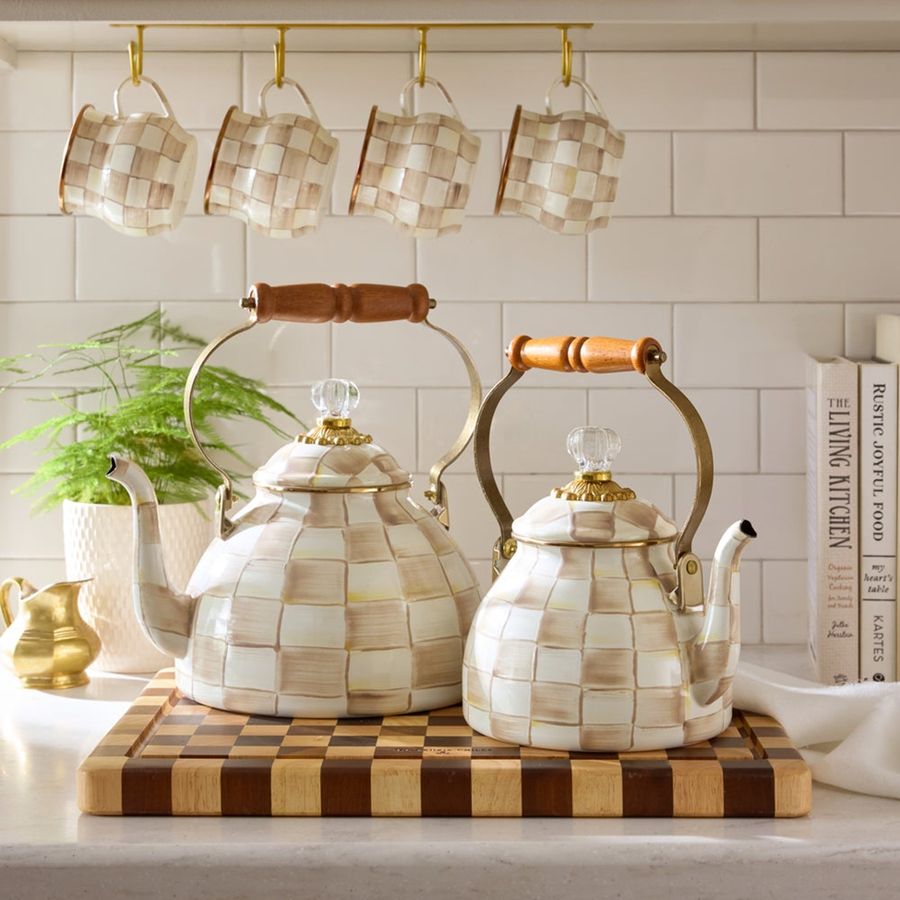 Decorative teapots with checkered pattern on a wooden cutting board in a kitchen setting.