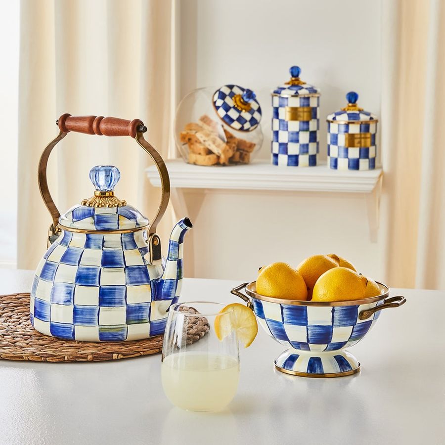 Blue and white checkered teapot, colander with lemons, and glass on a table.