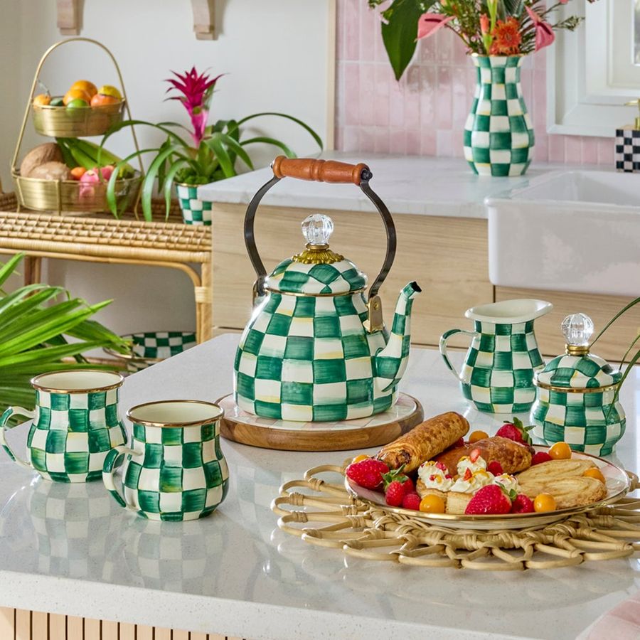 Green and white checkered teapot and mugs on a kitchen counter with a plate of food.
