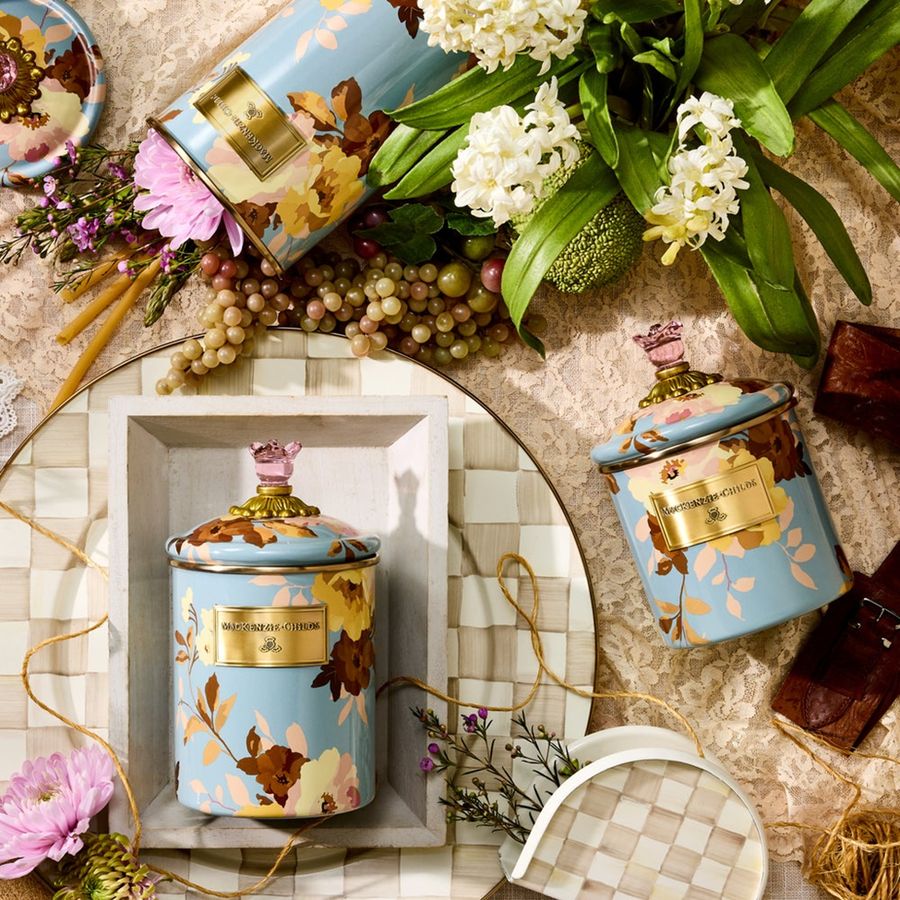 Decorative canisters with floral designs on a textured surface with flowers and chocolate.