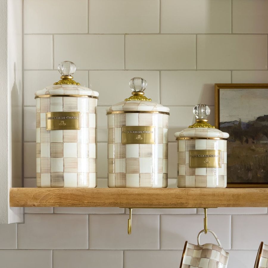 Set of three decorative jars with checkered patterns on a wooden shelf against a tiled wall.