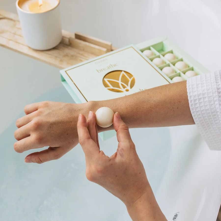 Person applying a white cream to their wrist with a book and candle in the background