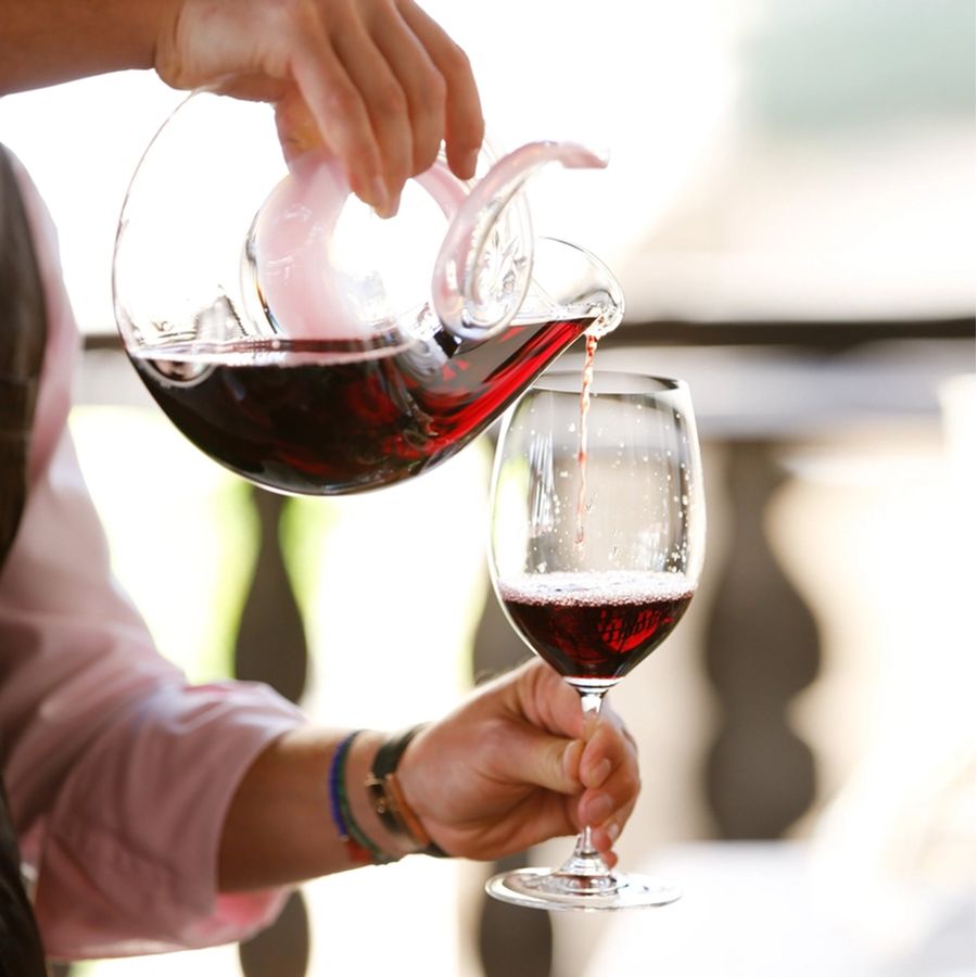 Hand pouring red wine from glass carafe into Reidel wine glass.