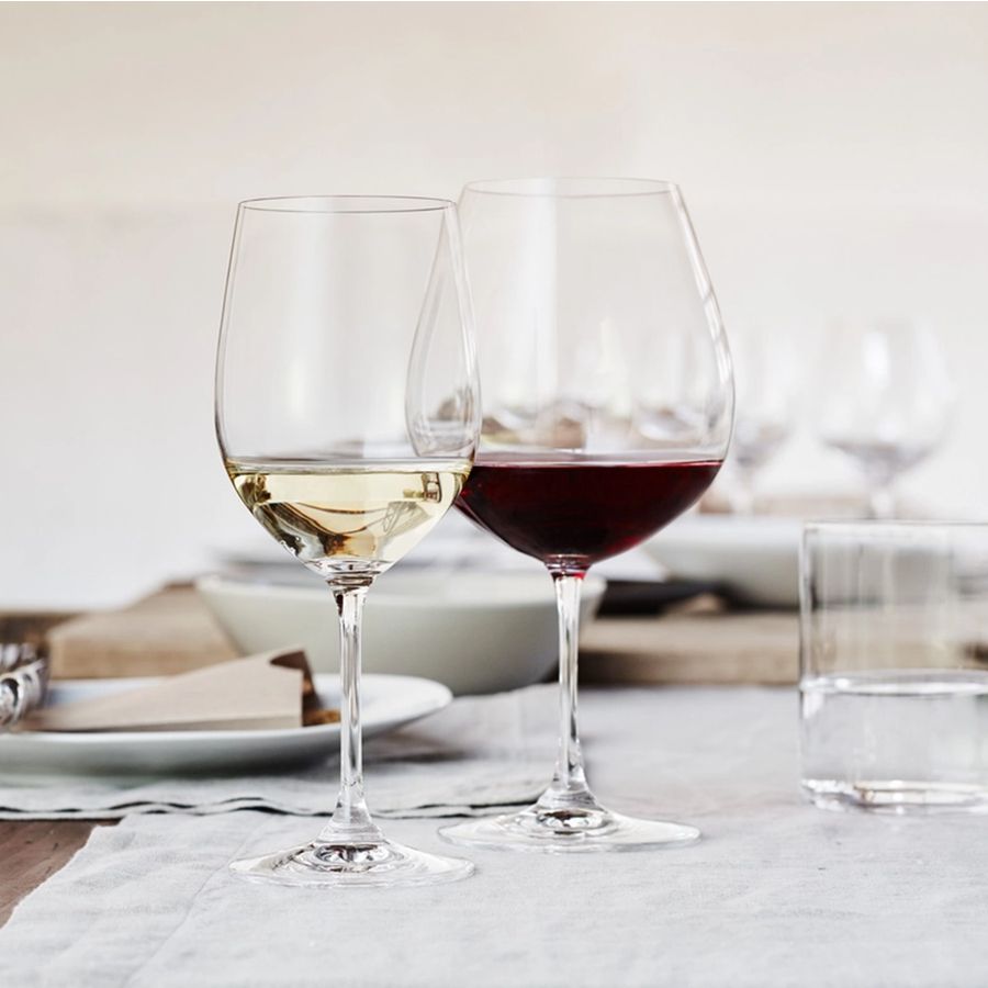 Reidel wine glasses holding white and red wine on a dining table.