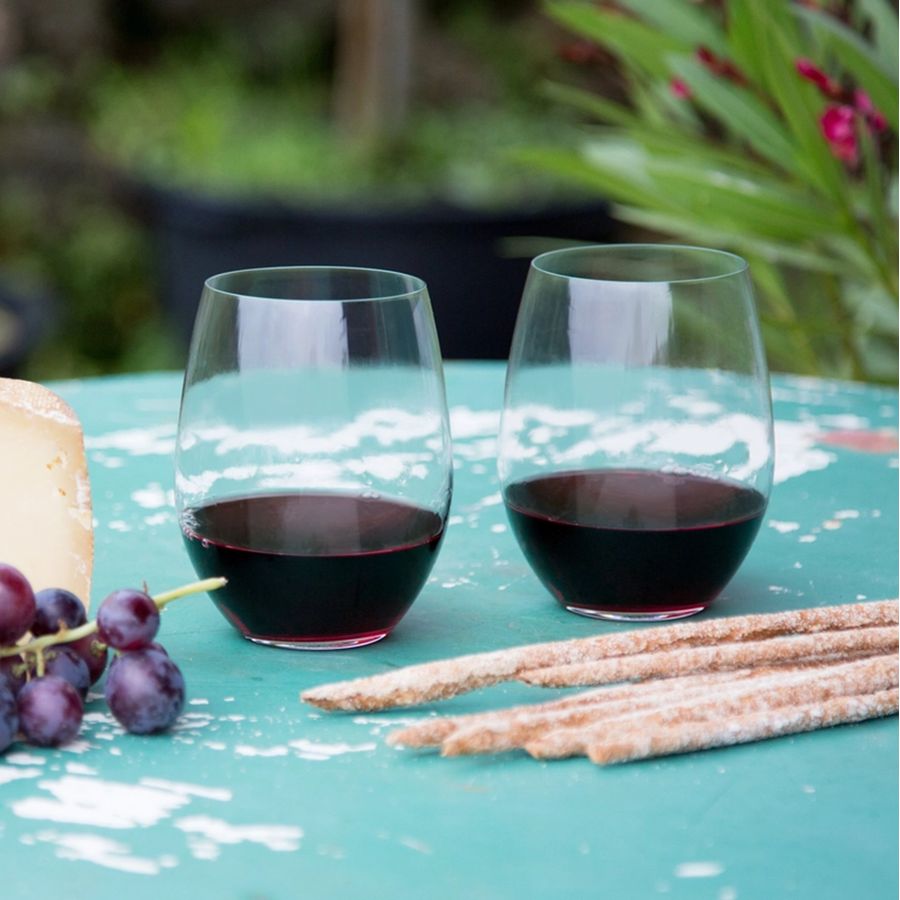 Reidel stemless wine glasses with red wine, grapes, cheese, and breadsticks on a teal table.
