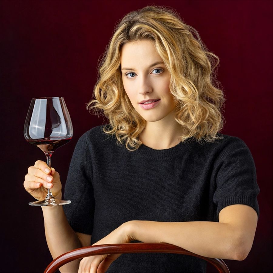 Reidel wine glass held by a woman with curly blonde hair against a deep red background.