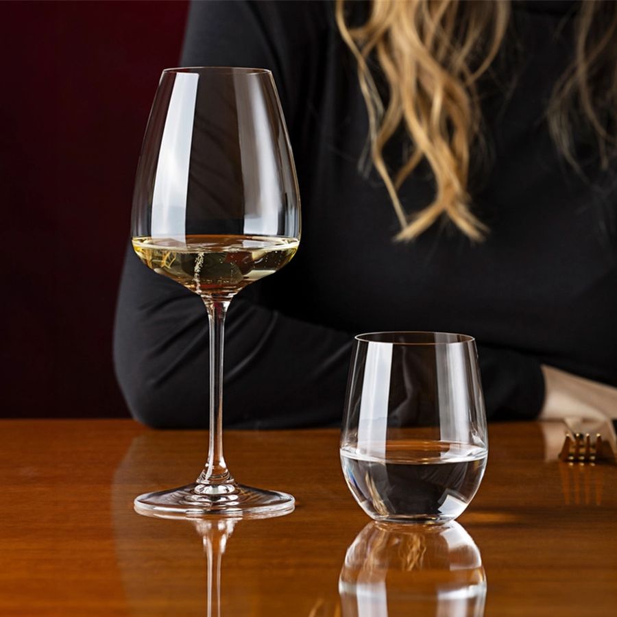 Reidel wine glasses, one tall with white wine, one short with water, on wooden table.