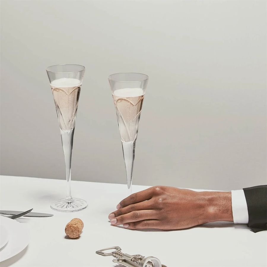 Two champagne flutes with a cork and silver bottle opener on a white surface.